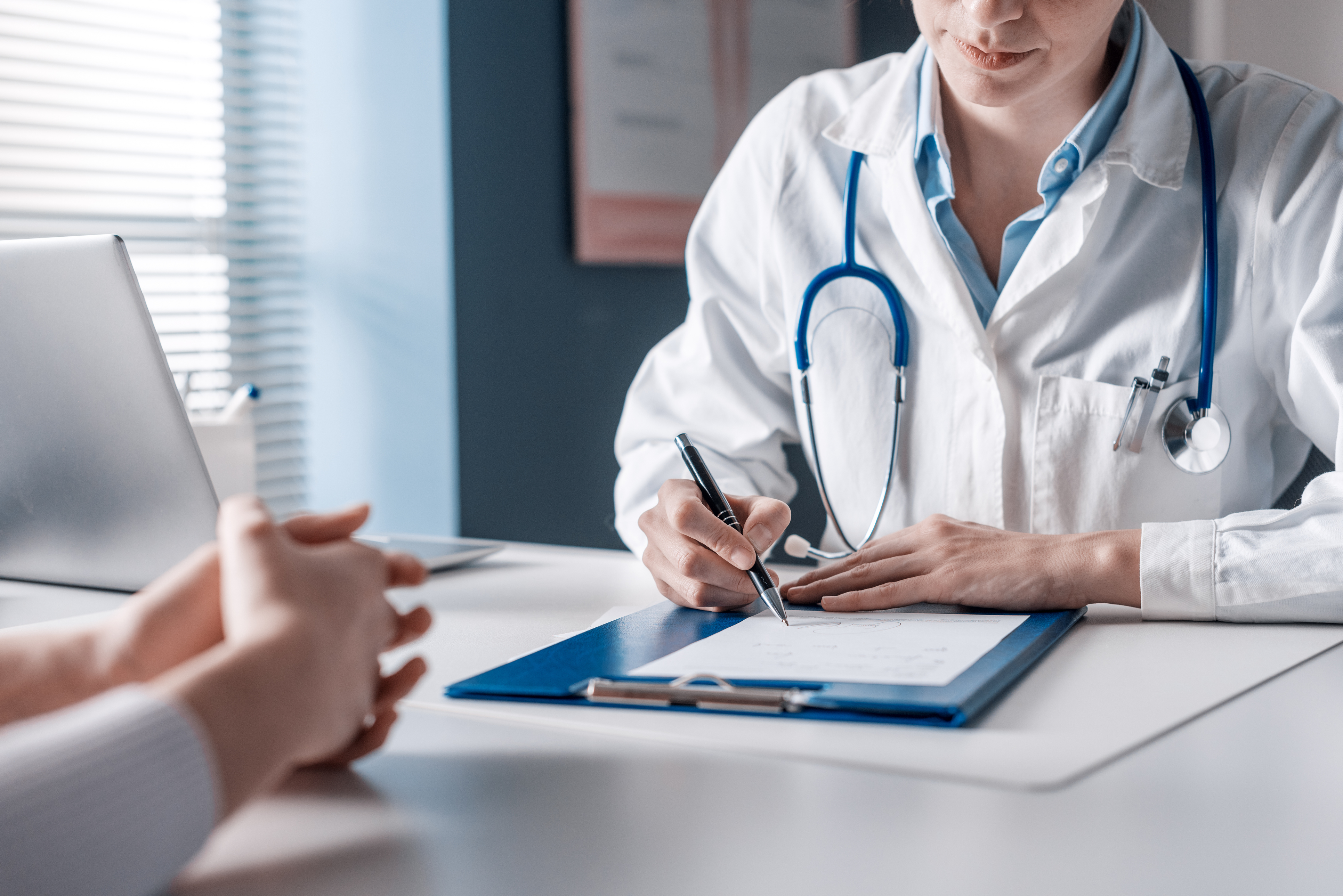 Focus su medico donna con al collo uno stetoscopio mentre prescrive una ricetta a una scrivania